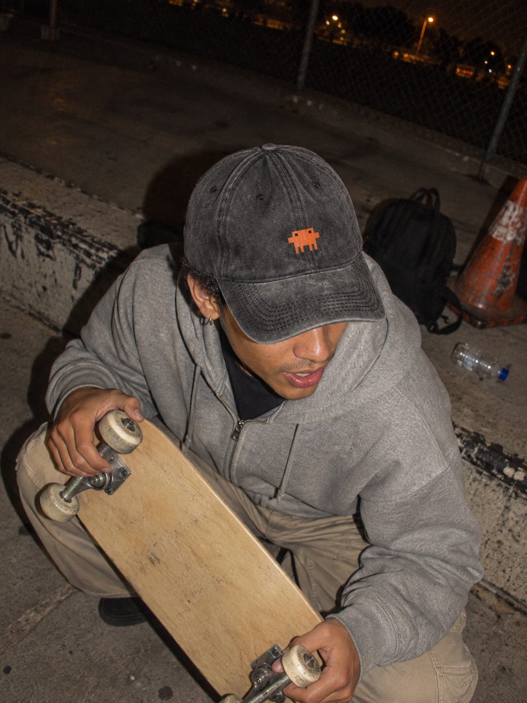 Rapaz agachado numa pista de skate à noite, de boné Pixelguejo preto